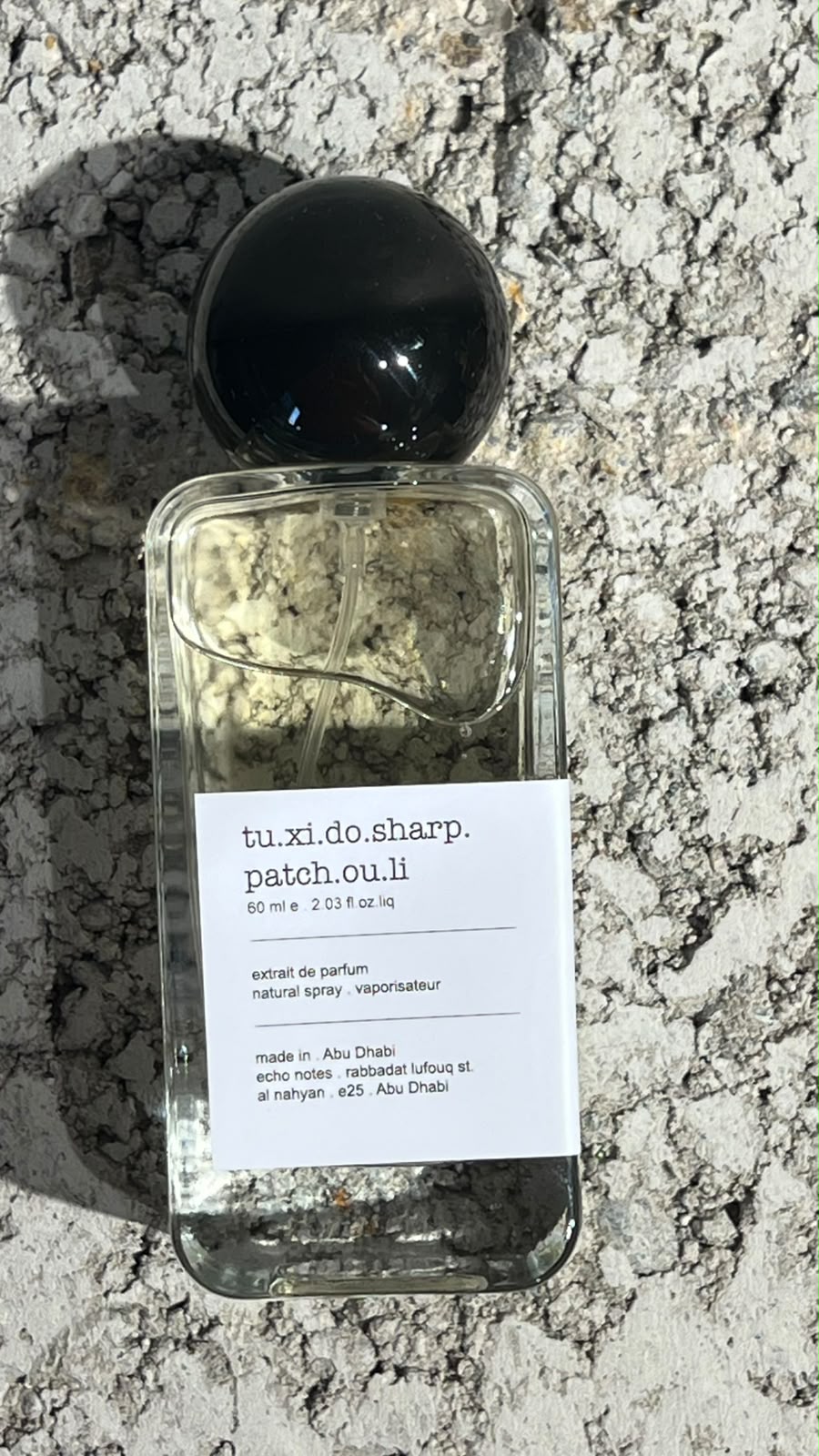 Echo Notes Tuxedo Sharp Patchouli perfume bottle framed by fresh violet leaves, black pepper, and dark patchouli.