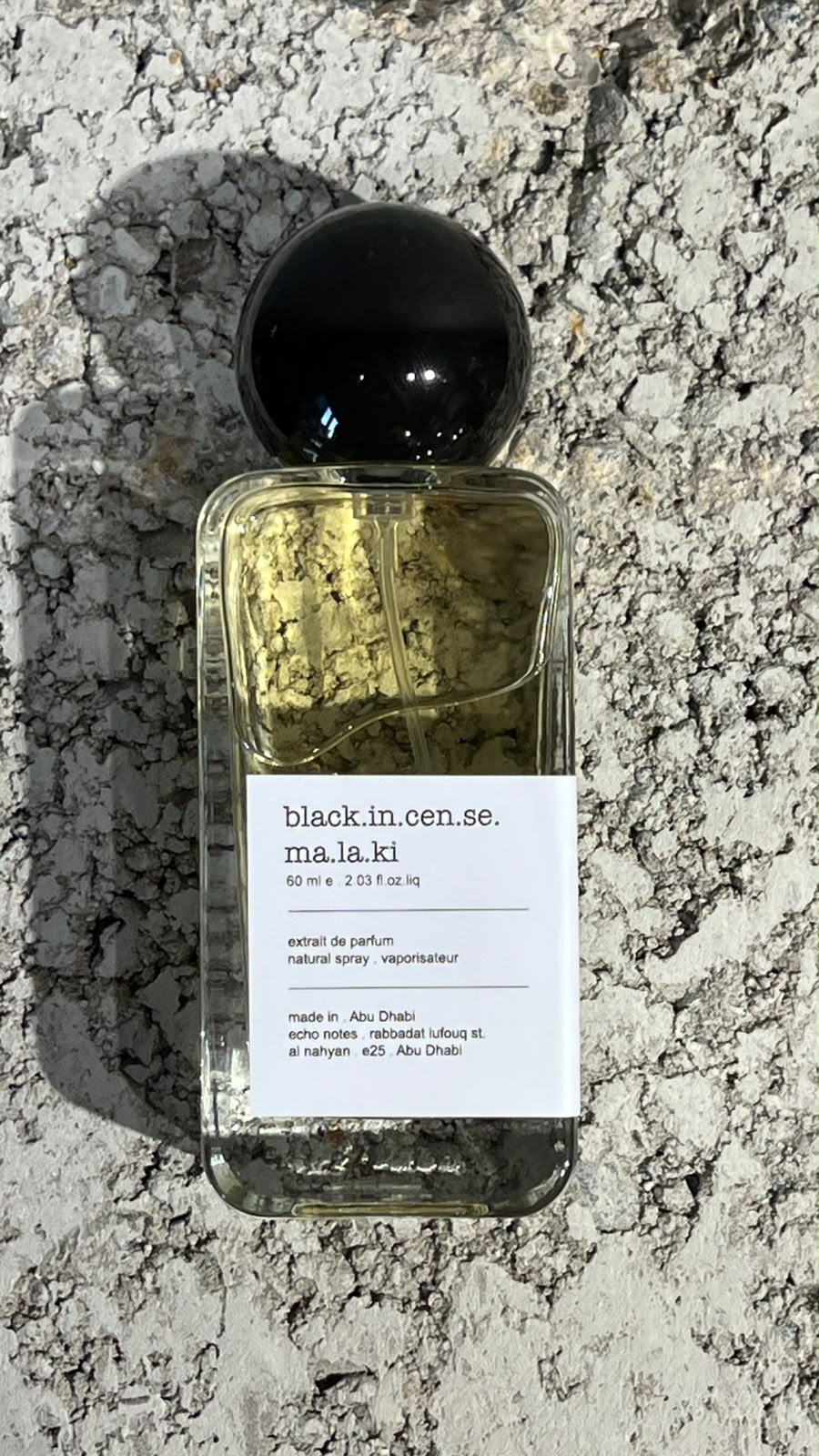 Echo Notes Black Incense Malaki perfume bottle surrounded by a piece of leather, rising incense smoke, oud chips, and olibanum resin.