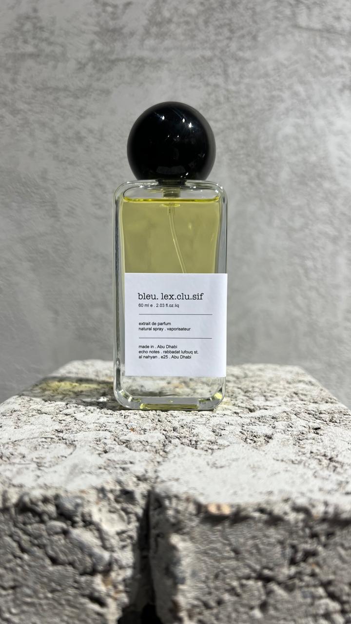 Echo Notes Bleu L’Exclusif perfume bottle surrounded by fresh bergamot, juniper berries, cardamom pods, black peppercorns, and cedar.