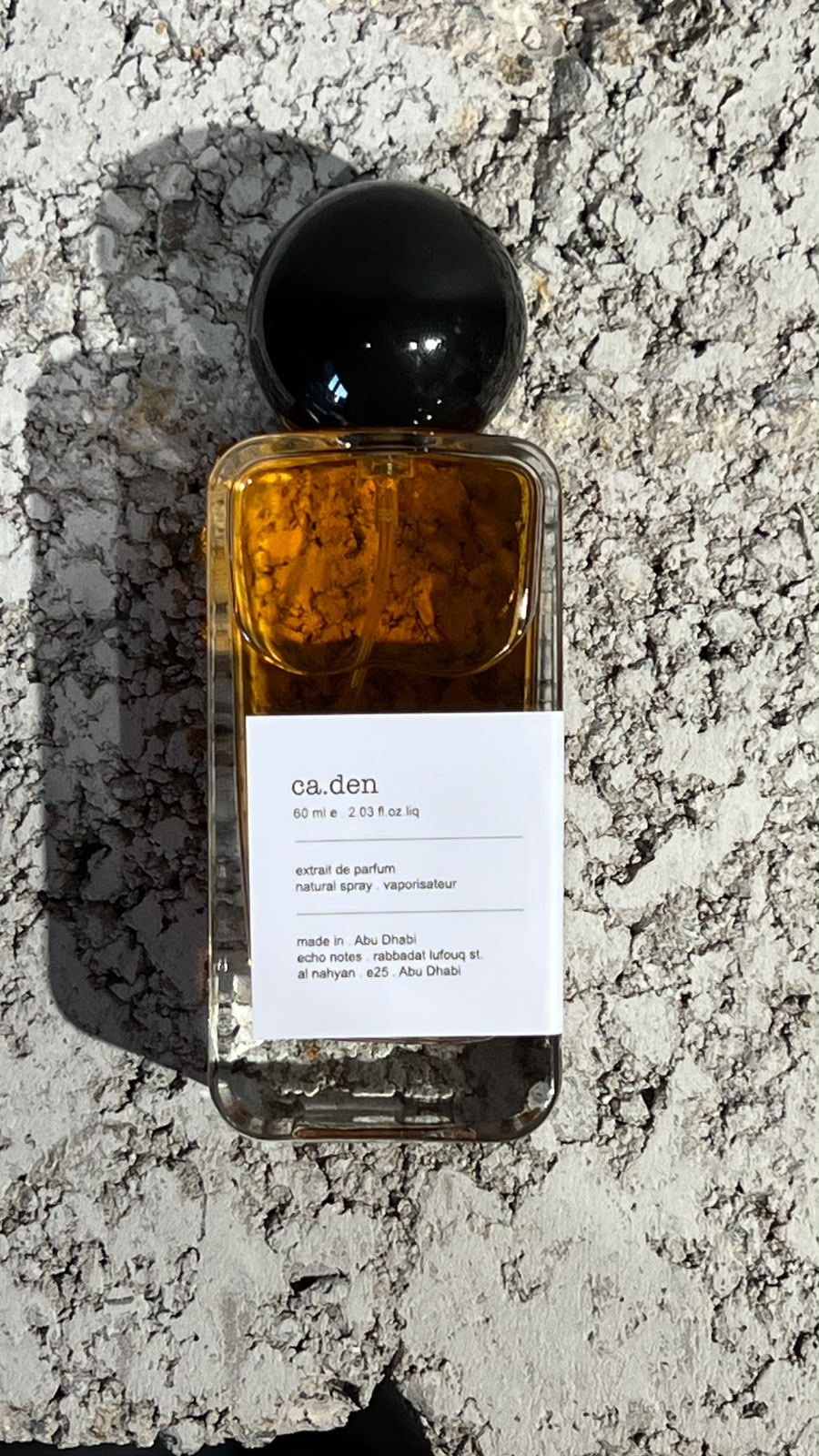 Echo Notes Caden perfume bottle surrounded by saffron threads, cardamom pods, amber liquor, soft suede, and coffee beans.