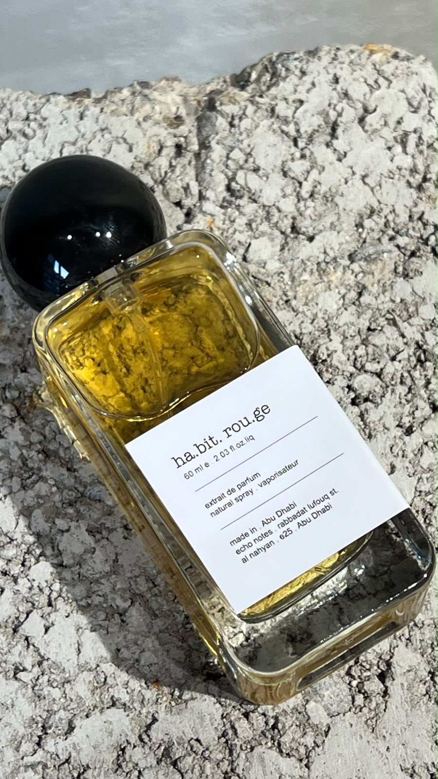 Echo Notes Habit Rouge perfume bottle surrounded by vanilla pods, amber rum, dried patchouli leaves, and fresh bergamot.
