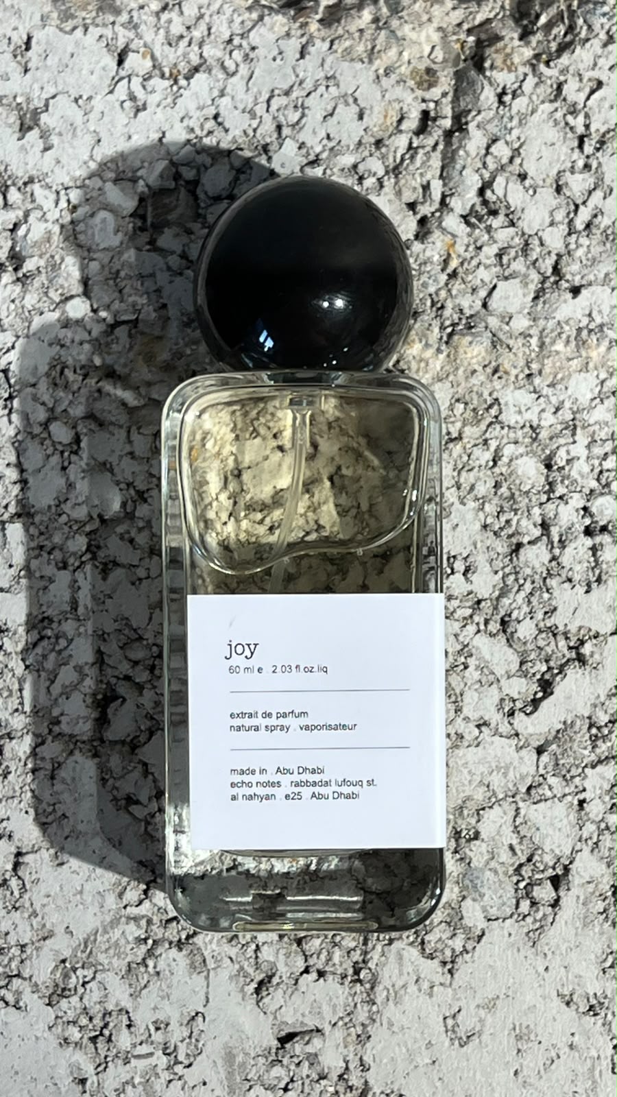 Echo Notes Joy perfume bottle surrounded by sparkling bergamot, Grasse rose petals, and soft white musk.