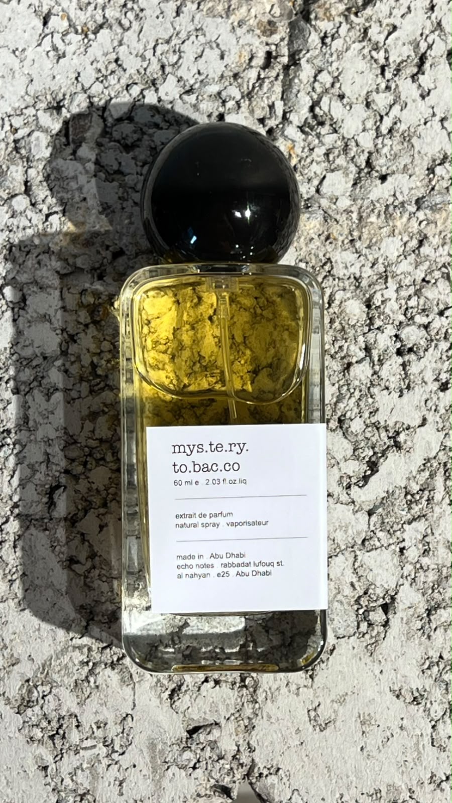 Echo Notes Mystery Tobacco perfume bottle surrounded by golden osmanthus blossoms, cured tobacco leaves, and tonka beans.