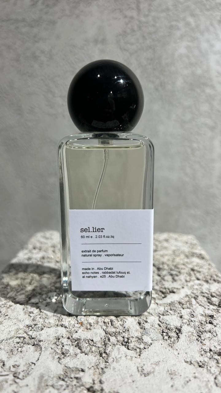 Echo Notes Sellier perfume bottle surrounded by black tea leaves, soft cashmeran fabric, dark leather, birch, and oakmoss.